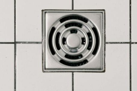 Natural Drain Cleaners - Top view of white ceramic tile floor with stainless steel square shaped cover of drain in contemporary shower