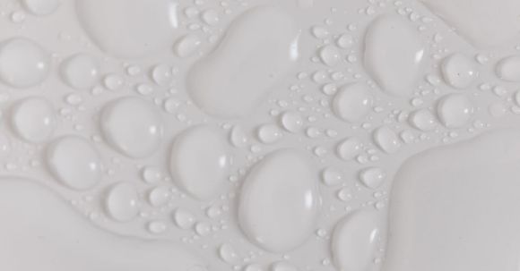 Water Leak Sounds - Closeup top view of wet plain white background of droplet with translucent clean still water drops of different shapes and sizes